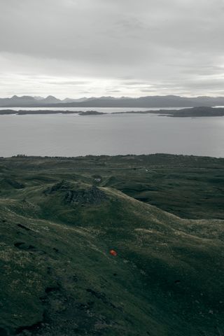 View from a hill of a loch in Scotland with a red camping tent setup down of the hill