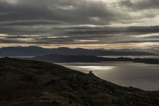 Landscape view from a hill of scottish lochs with a raising sun piercing the clouds