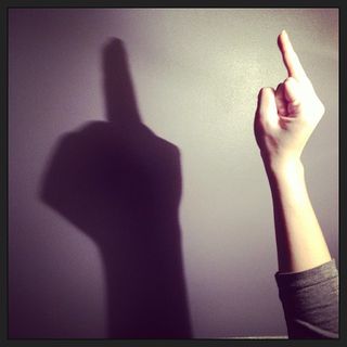 An arm raising the middle finger with its shadow on the wall behind