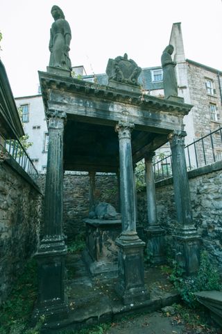 An opulent tombstone, much like a temple, with columns and a roof enclosed in a small area with walls