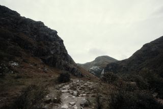 A rocky path between mountains and a cloudy whitish sky beyond