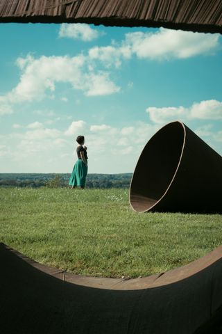 A woman in a green skirt on a lawn next to a cone and seen through a cone