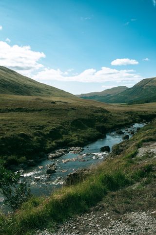 Landscape of scottish valley with mountains in the background and a river in the foreground on a sunny day