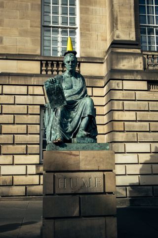 Statue of David Hume in Edinburgh with a yellow traffic cone on the head