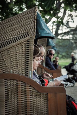 Line up of people sitted in rattan booths in a public garden with one of those people looking at the camera