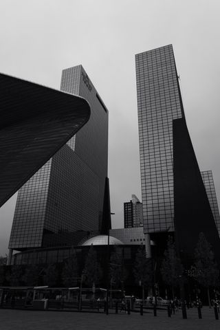 Black and white picture of tall and straight buildings in the back and curvy structure photobombing