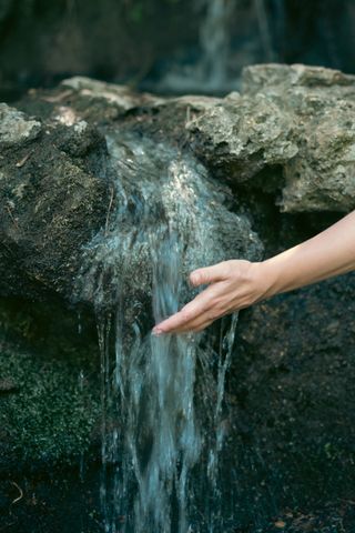 A woman's hand feeling the water of a small cascade through her fingers