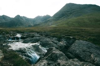 A stream of water gently going down in the foreground with mountains and a bright sun in the background