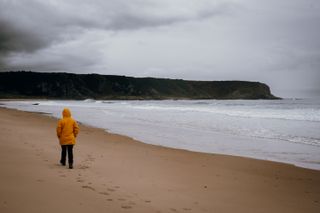 A person in a yellow raincoat walking on a beach on a stormy weather